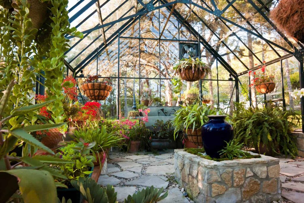 The inside of a greenhouse with a stone floor surrounded by pots of plants.
