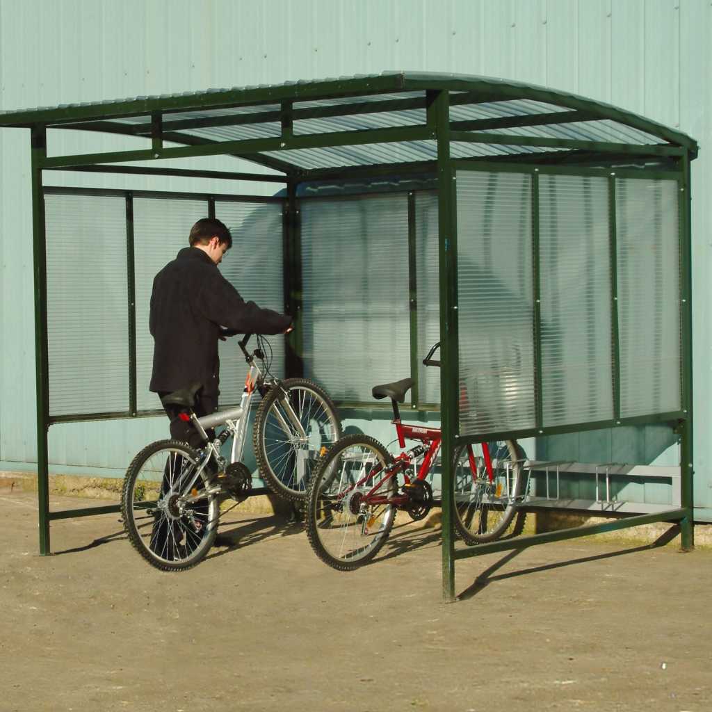 A man with two bikes underneath a cycle shelter made from twinwall polycarbonate.