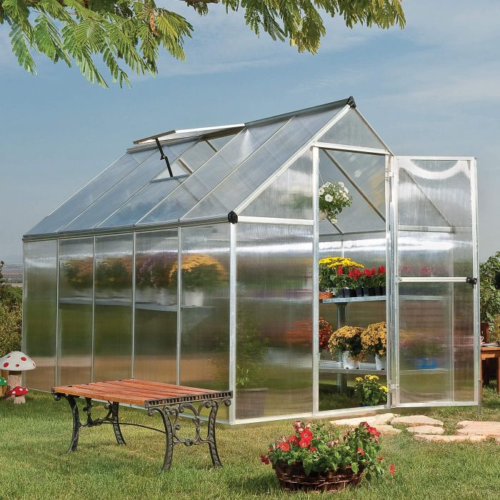 A twinwall polycarbonate greenhouse with plants and a bench next to it.